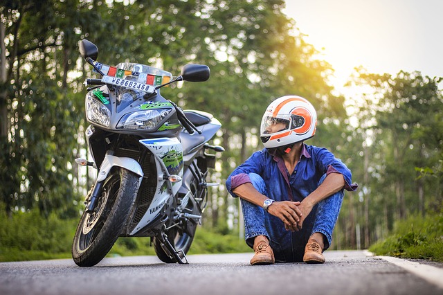 Muž sedí na ceste vedľa svojej motorky, moto-prilba