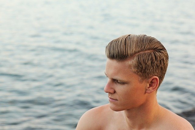 Chlapec s blond vlasmi stojí pri vode.jpg